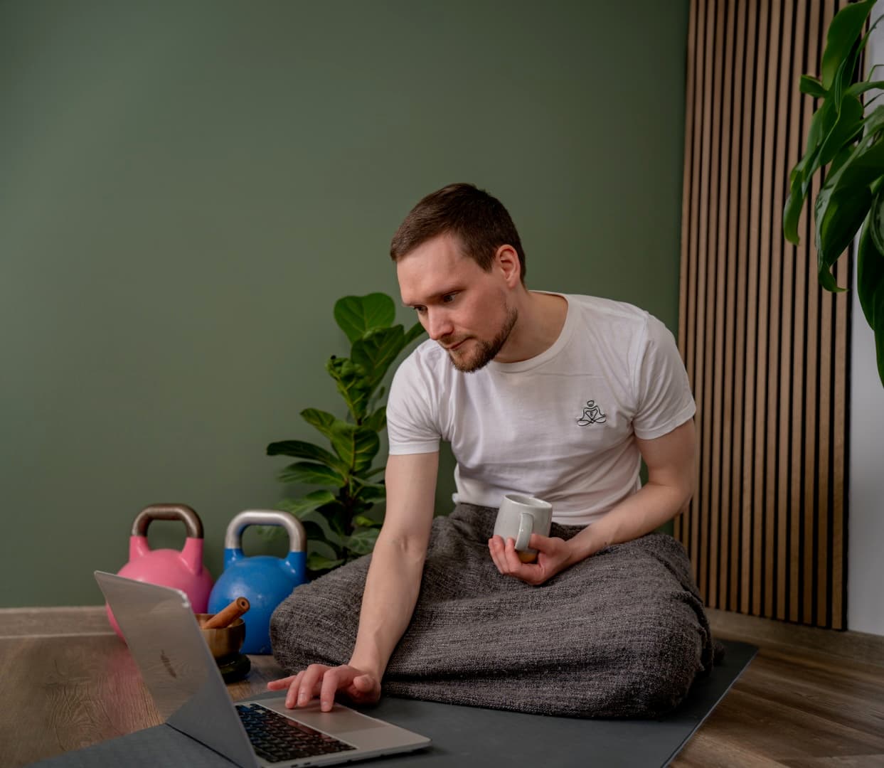 Entspannungshelden Gründer Johannes - Online Entspannungskurse & Stressmanagement Training Entspannungstrainer Johannes bei Online-Coaching Session mit Laptop und Kaffee, umgeben von Trainingsgeräten und Zimmerpflanzen in entspannender Atmosphäre